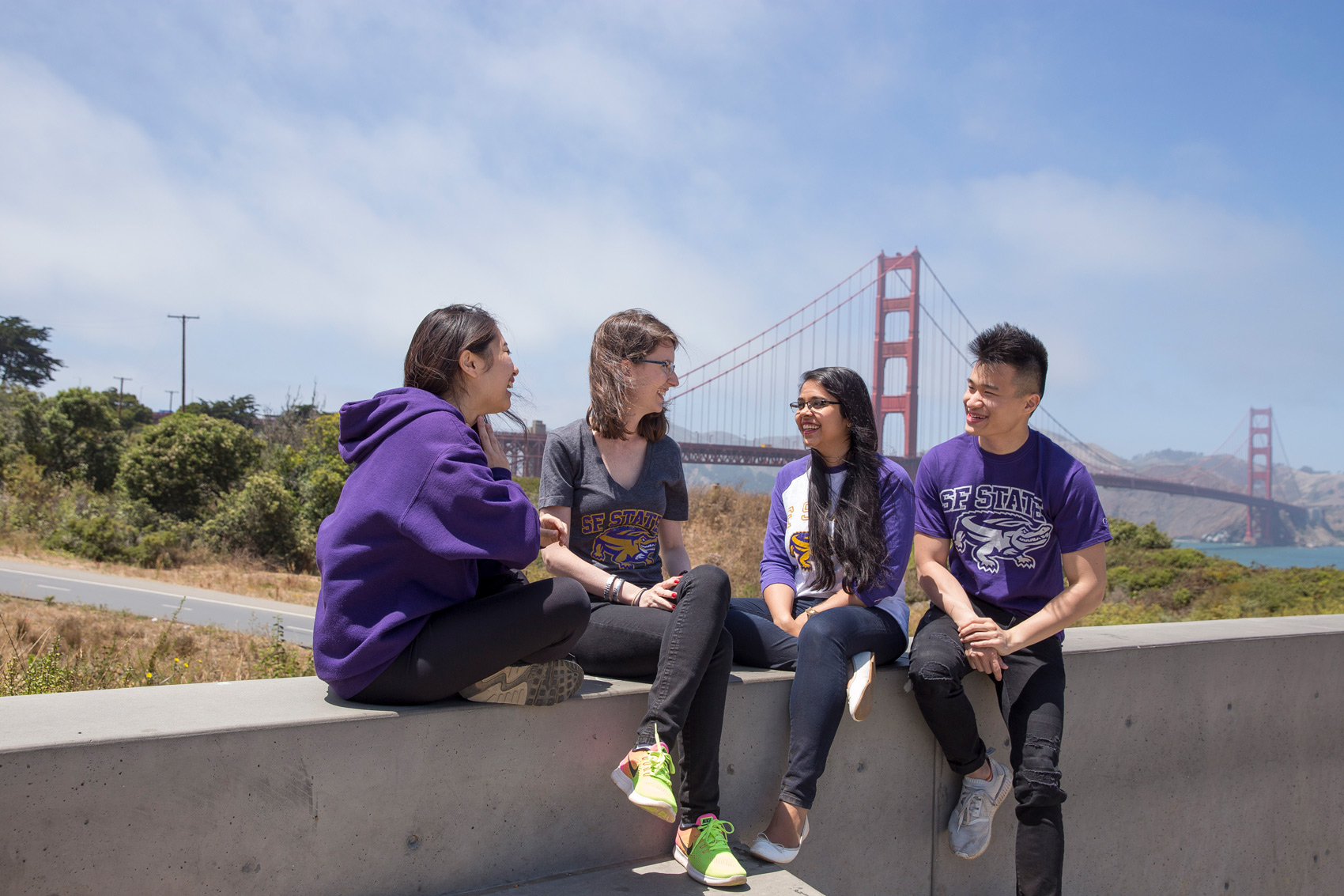 Four happy SF State students sitting having a conversation with the Golden Gate Bridge in the background