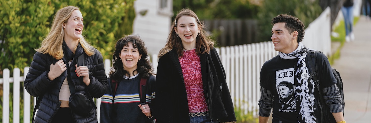 Four students walking and smiling outside near campus housing