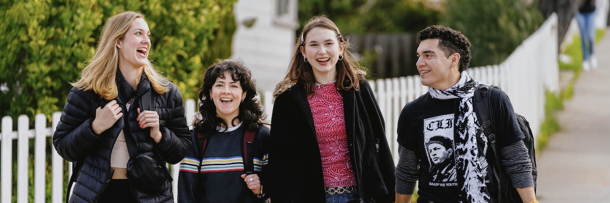 Four students walking and smiling outside near campus housing
