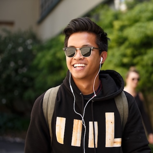 male student walking on campus listening to headphones and wearing sunglasses